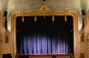 Purple curtains are drawn across a stage framed by an opulent gold frame.