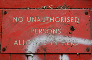 A red sign on a painted red wall that reads, 'No unauthorised persons allowed in here' in white text styled in all capital letters.