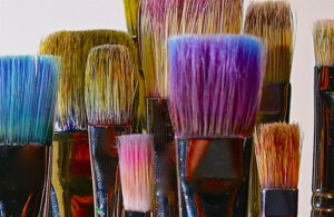 Paint brushes with blue, pink, purple and yellow in the bristles.