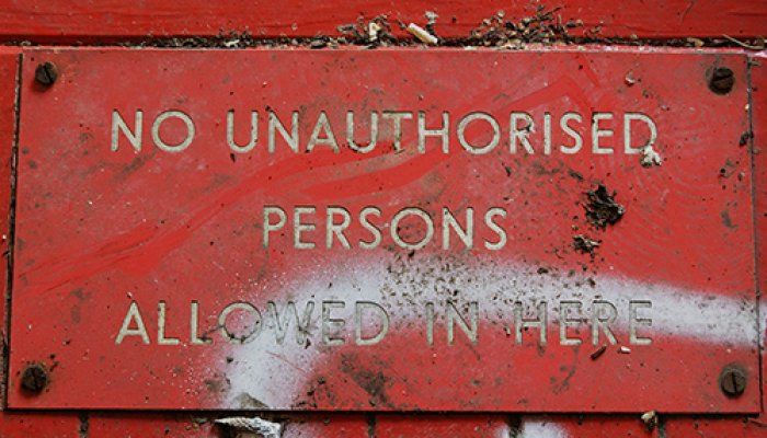 A red sign on a painted red wall that reads, 'No unauthorised persons allowed in here' in white text styled in all capital letters.