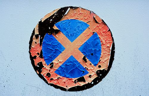 A peeling sticker with a red circle and an x crossed over a blue background.