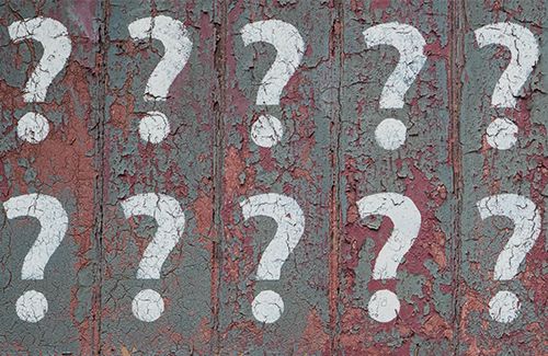 10 white question marks stenciled onto a grey-green wall. The grey-green paint is peeling revealing maroon paint underneath.