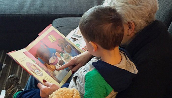 A grandmother and her grandson sit together reading a picture book.